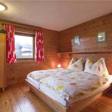 Ein gemütliches Schlafzimmer mit Holzvertäfelungen. Es gibt ein Doppelbett, einen Kleiderschrank und bunten Vorhängen.