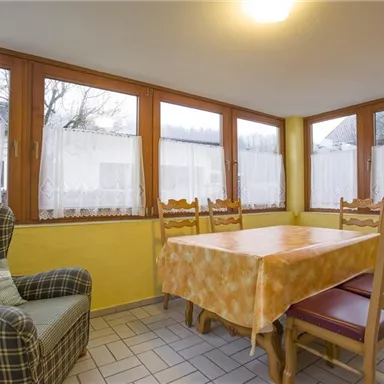 Ein gemütlicher Essbereich mit einem großen Tisch und Stühlen. Die Wände sind gelb gestrichen und die Fenster lassen viel Licht herein.