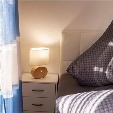 Ein stilvolles Schlafzimmer mit einem großen Kissen und einem Nachttisch. Neben dem Nachttisch steht eine elegante Lampe, die sanftes Licht spendet.