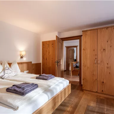 Ein gemütliches Schlafzimmer mit einem Doppelbett und holzvertäfelten Wänden. Es gibt einen Kleiderschrank und weiche Handtücher auf dem Bett.