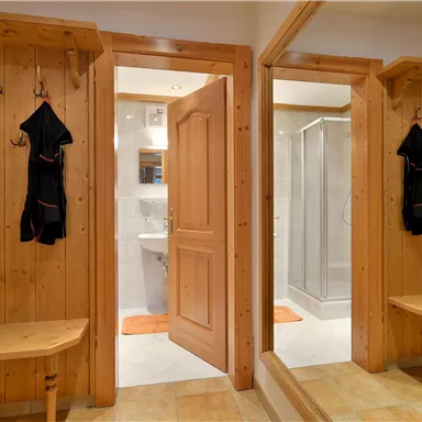 A cozy entrance area with wooden paneling and a mirror. In the background, a bathroom with a shower is visible.