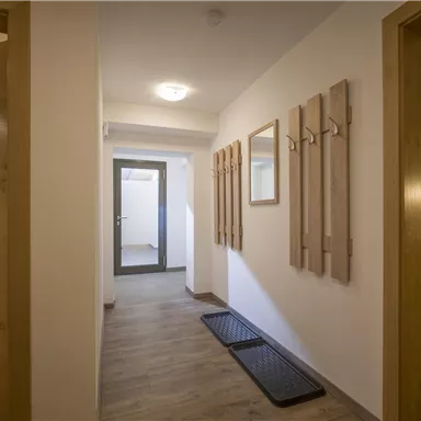 Ein heller Flur mit Holzdetails und modernen Aufhängemöglichkeiten. Auf der linken Seite sind Türen zu angrenzenden Räumen sichtbar.
