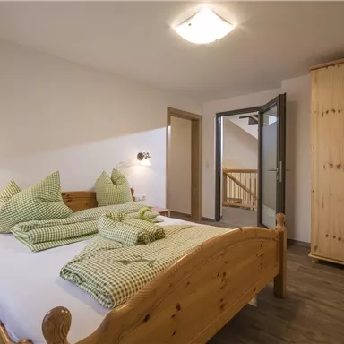 Ein gemütliches Schlafzimmer mit einem Holzbett und grünen Kissen. Der Raum hat einen Kleiderschrank aus Holz und viel Tageslicht.