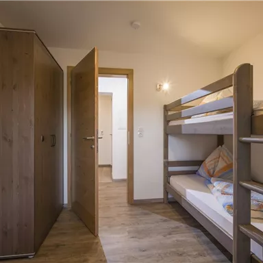 Ein einfaches Schlafzimmer mit einem Etagenbett und einem Kleiderschrank. Die Wände sind hell und der Boden ist aus Holz.