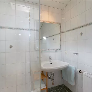 Ein modernes Badezimmer mit einer Dusche und einem Waschbecken. Die Wände sind fliesenverkleidet und es gibt eine große Spiegel.