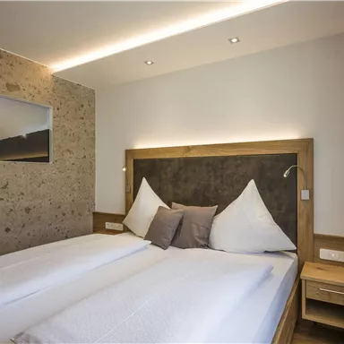 A modern bedroom with a double bed and clean lines. There is a large mirror and a warm color palette.
