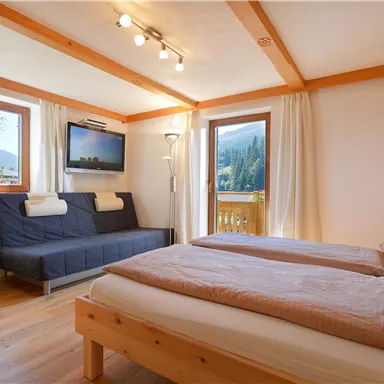 A cozy room with two beds and a sofa bed. Large windows offer a view of the mountains and plenty of daylight.