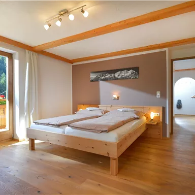 A cozy bedroom with two beds and wooden ceilings. Large windows let in plenty of light and offer a view of nature.