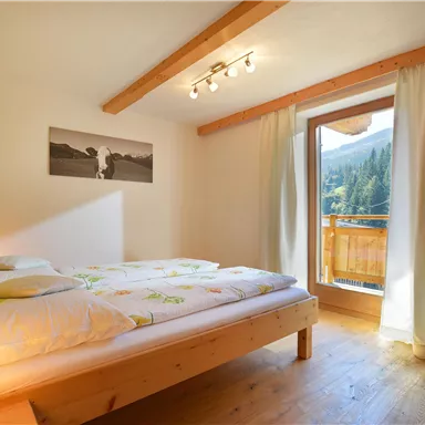 A cozy bedroom with a double bed and wooden paneling. A large window front offers a view of the mountains.