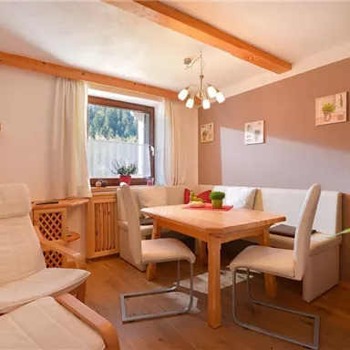 A cozy dining area with a square wooden table and bright chairs. Decorative pictures hang on the wall, and the room is well-lit.
