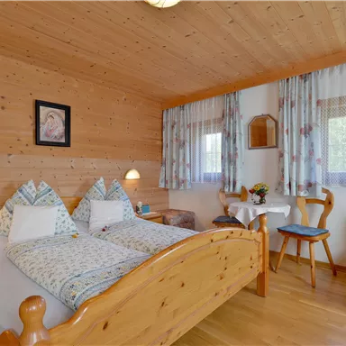 A cozy bedroom with wooden paneling and two beds. The room is bright and inviting, with a small table and chairs.