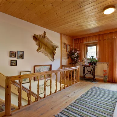 A cozy entrance area with wood paneling and a staircase. Various pictures hang on the walls, and a window lets in a lot of light.