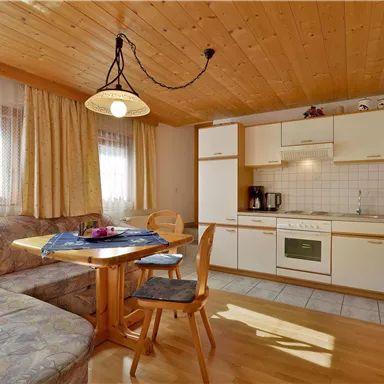 A cozy kitchen with a wooden dining area and a sofa. The walls are light and the room is well-lit.