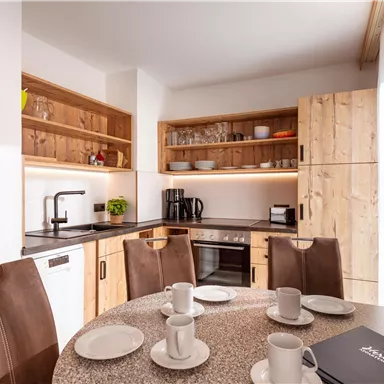 A modern kitchen with wooden shelves and an elegant countertop. The table is set with cups and plates, ideal for a meal.