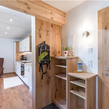 Ein heller Eingangsbereich mit Holzverkleidung und einem offenen Blick auf die Küche. Ein Schuhregal und eine Garderobe sind zu sehen.