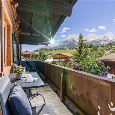 Ein einladender Balkon mit Blick auf die Berge. Bunte Blumen und eine sonnige Atmosphäre schaffen eine entspannte Umgebung.