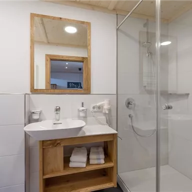 Ein modernes Badezimmer mit einer Duschkabine und einem Waschbecken aus Holz. Der Raum ist hell und minimalistisch gestaltet.