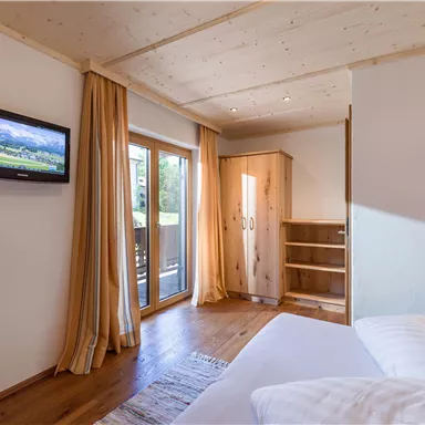 Ein gemütliches Schlafzimmer mit einem großen Fenster und einem Fernseher an der Wand. Die Einrichtung ist modern und hell mit Holz-Elementen.
