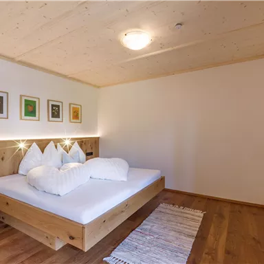 Ein modernes Schlafzimmer mit einem großen Bett und hellen Holzdetails. Die Wände sind geschmückt mit kunstvollen Bildern, und das Zimmer hat einen ruhigen, einladenden Charakter.