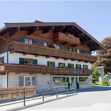 Ein charmantes Gebäude im alpinen Stil mit Balkonen und holzverkleideter Fassade. Es steht an einer ruhigen Straße in einer malerischen Umgebung.