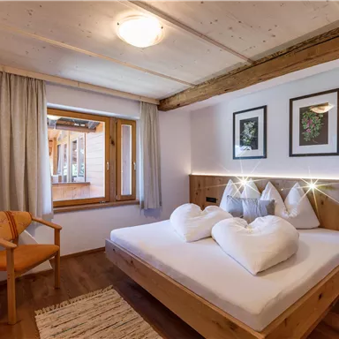 Ein gemütliches Schlafzimmer mit einem großen Bett und herzförmigen Kissen. Die Wände sind hell, und es gibt einen schönen Ausblick durch das Fenster.