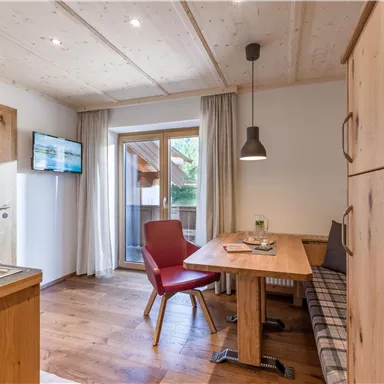 Ein gemütlicher Raum mit Holzverkleidung und einem Tisch. Es gibt einen Fernseher und einen Balkon mit Blick ins Freie.