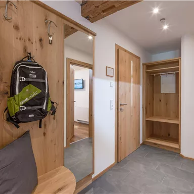 Ein moderner Flur mit Holzpaneelen und einem großen Spiegel. An der Wand hängt ein Rucksack, und es gibt Platz für Kleidung und Schuhe.