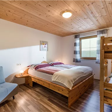 Ein gemütliches Schlafzimmer mit einem Doppelbett und einem Hochbett. Es gibt einen Sessel und ein Fenster mit Blick nach draußen.