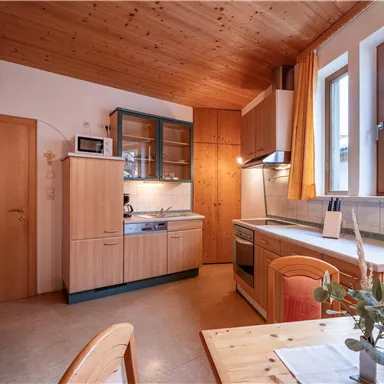 A cozy kitchen with wooden surfaces and large windows. The table is decorated with a plant, creating an inviting atmosphere.