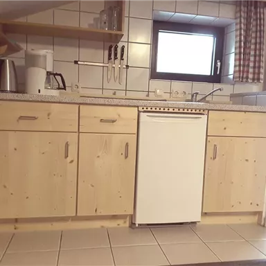 A modern kitchen with wooden cabinets and ceramic tiles. It is well equipped with a refrigerator and various kitchen utensils.