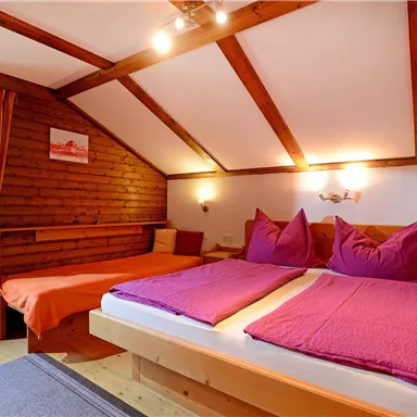 A cozy bedroom with two beds and purple bedding. Wooden walls and large windows create an inviting atmosphere.