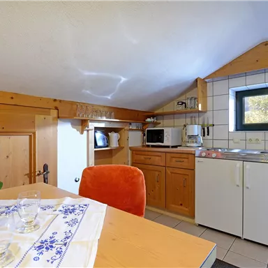 A cozy kitchen with wooden shelves and modern appliances. A table with floral decoration invites you to linger.