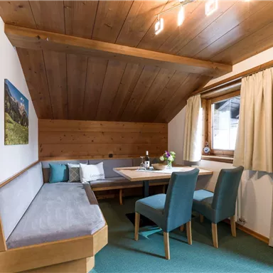 A cozy dining area with wooden paneling and a large table. The blue chairs and the view of the window create an inviting atmosphere.