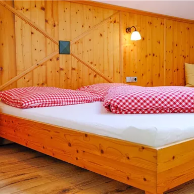 A cozy bedroom with a wooden bed and checkered red cushions. Wooden walls give the room a warm atmosphere.
