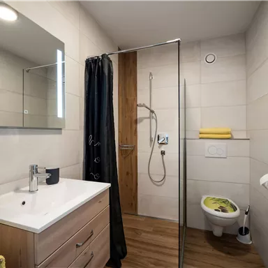 Ein modernes Bad mit einer Dusche und einem Waschbecken. Es gibt helle Fliesen und Holz-Elemente, sowie farbige Handtücher.