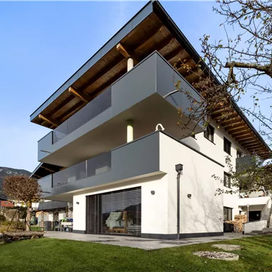 Ein modernes Wohnhaus mit mehreren Balkonen und einer klaren, minimalistischen Fassade. Die grüne Wiese und die umliegende Landschaft schaffen eine einladende Atmosphäre.