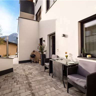Eine moderne Terrasse mit einem Tisch und Sesseln. Im Hintergrund sind Berge und ein klarer Himmel zu sehen.