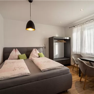 Ein gemütliches Schlafzimmer mit einem Doppelbett und modernem Dekor. Der Raum ist hell und einladend, mit einem Schreibtisch und großem Fenster.