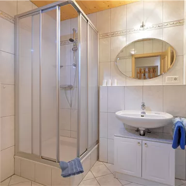 A modern bathroom with a shower cabin and a sink. Blue towels and decorative elements give the space an inviting atmosphere.