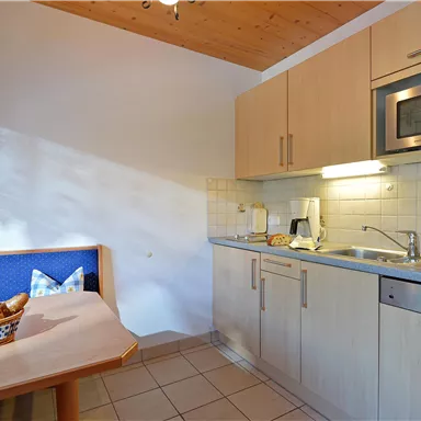 A modern kitchen with wooden details and a table. On the table lies a basket of rolls.