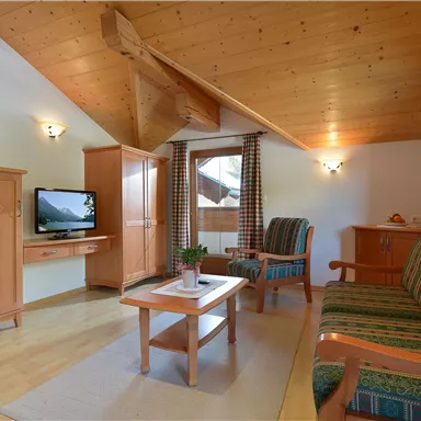 A cozy living room with wooden ceilings and modern furniture. It features a sofa, a coffee table, and a television.