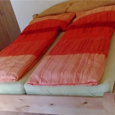 A bedroom with a wooden bed and orange bedspreads. The room is bright and has a simple, cozy style.