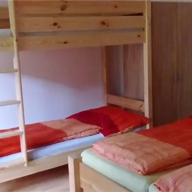 A cozy sleeping area with a wooden loft bed and a single bed. Both beds are equipped with red and orange bedspreads.