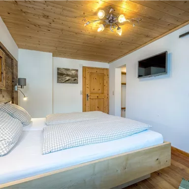 Ein gemütliches Schlafzimmer mit Holzdetails und einem großen Bett. Es gibt einen Fernseher an der Wand und einen Zugang zum Badezimmer.