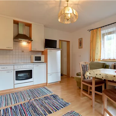 A bright kitchen with a dining table and chairs. The room is cozy and well-equipped, with a rug and large windows.