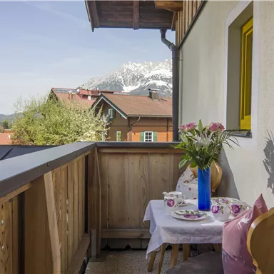 Ein schöner Balkon mit Holzgeländer und Blick auf die Berge. Auf dem Tisch stehen Blumen und Teetassen, ideal zum Entspannen.