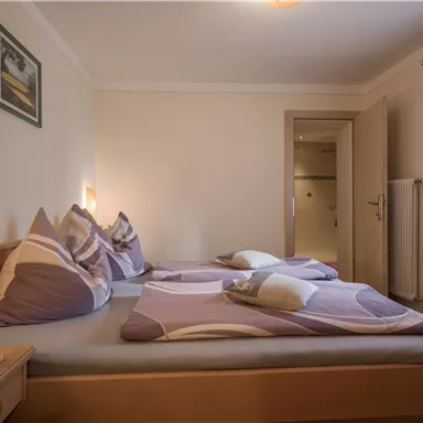 Ein gemütliches Schlafzimmer mit zwei Betten und bunten Kissen. Das Licht ist sanft und die Wände sind in neutralen Farben gestaltet.