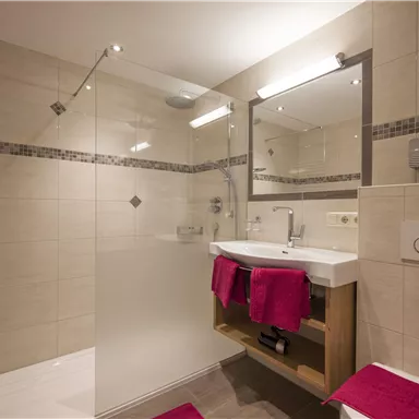 Ein modernes Badezimmer mit einer Glasdusche und einem Waschbecken. Rosa Handtücher und elegante Fliesen verleihen dem Raum eine einladende Atmosphäre.