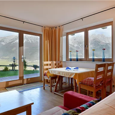 Ein gemütlicher Wohnraum mit Blick auf die Berge. Die großen Fenster lassen viel Licht herein und schaffen eine einladende Atmosphäre.