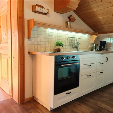 A modern kitchen with a white kitchen unit and a black stove. The wood decor and warm lighting give the kitchen a cozy atmosphere.